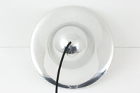 デンマークを代表する照明デザイナーVerner Panton(バーナー・パントン)が手がけた、Frandsen Lighting(フランセン・ライティング)社製のペンダントライトです。なだらかな曲線を描くベル型のシルエットに、ミラーのように周囲を映し出すクローム仕上げが施された、存在感のある一灯。直径約30cmと比較的大ぶりなサイズ感で、1灯でも空間のアクセントとなり、テーブル上や吹き抜け空間などにも映えます。内側はホワイトに塗装されており、点灯時には光を柔らかく広げながらもしっかりとした明るさを確保。Frandsen Lighting社はかつてVerner Pantonとのライセンス契約を結び、このモデルを製造していましたが、現在ではその契約も終了しており、本品のようなオリジナルはヴィンテージ品でしか手に入らなくなっています。特に直径30cmの大きなサイズは現行品では展開されておらず、希少性の高いアイテムとなっています。