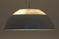 デンマークを代表する建築家・デザイナー、アルネ・ヤコブセンによってデザインされた「AJロイヤル」ペンダントライト。Louis Poulsen(ルイスポールセン)社より発表され、建築物と調和するミニマルなフォルムが特徴的です。こちらは直径50cmのホワイトカラーのモデルで、1958年に設計されたコペンハーゲンのSASロイヤルホテルのために開発されたシリーズのひとつ。上部のルーバー構造からも光が漏れる設計により、下方向だけでなく柔らかく空間全体を照らします。モダニズムの美学が息づく名作照明でありながら、日常の空間にもすっと馴染む柔らかな存在感が魅力です。ヴィンテージ品のため、シェードには擦り傷や小さな塗装剥がれ、内側に若干のサビが見られますが、使用には問題ありません。全体としては良好なコンディションを保っており、ヴィンテージならではの風合いをお楽しみいただけます。コードおよびソケットは国内基準に適合した仕様に交換済みで、すぐにご使用いただけます。