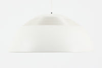 デンマークを代表する建築家・デザイナー、アルネ・ヤコブセンによってデザインされた「AJロイヤル」ペンダントライト。Louis Poulsen(ルイスポールセン)社より発表され、建築物と調和するミニマルなフォルムが特徴的です。こちらは直径50cmのホワイトカラーのモデルで、1958年に設計されたコペンハーゲンのSASロイヤルホテルのために開発されたシリーズのひとつ。上部のルーバー構造からも光が漏れる設計により、下方向だけでなく柔らかく空間全体を照らします。モダニズムの美学が息づく名作照明でありながら、日常の空間にもすっと馴染む柔らかな存在感が魅力です。ヴィンテージ品のため、シェードには擦り傷や小さな塗装剥がれ、内側に若干のサビが見られますが、使用には問題ありません。全体としては良好なコンディションを保っており、ヴィンテージならではの風合いをお楽しみいただけます。コードおよびソケットは国内基準に適合した仕様に交換済みで、すぐにご使用いただけます。