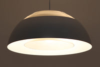 デンマークを代表する建築家・デザイナー、アルネ・ヤコブセンによってデザインされた「AJロイヤル」ペンダントライト。Louis Poulsen(ルイスポールセン)社より発表され、建築物と調和するミニマルなフォルムが特徴的です。こちらは直径50cmのホワイトカラーのモデルで、1958年に設計されたコペンハーゲンのSASロイヤルホテルのために開発されたシリーズのひとつ。上部のルーバー構造からも光が漏れる設計により、下方向だけでなく柔らかく空間全体を照らします。モダニズムの美学が息づく名作照明でありながら、日常の空間にもすっと馴染む柔らかな存在感が魅力です。ヴィンテージ品のため、シェードには擦り傷や小さな塗装剥がれ、内側に若干のサビが見られますが、使用には問題ありません。全体としては良好なコンディションを保っており、ヴィンテージならではの風合いをお楽しみいただけます。コードおよびソケットは国内基準に適合した仕様に交換済みで、すぐにご使用いただけます。