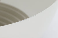 デンマークを代表する建築家・デザイナー、アルネ・ヤコブセンによってデザインされた「AJロイヤル」ペンダントライト。Louis Poulsen(ルイスポールセン)社より発表され、建築物と調和するミニマルなフォルムが特徴的です。こちらは直径50cmのホワイトカラーのモデルで、1958年に設計されたコペンハーゲンのSASロイヤルホテルのために開発されたシリーズのひとつ。上部のルーバー構造からも光が漏れる設計により、下方向だけでなく柔らかく空間全体を照らします。モダニズムの美学が息づく名作照明でありながら、日常の空間にもすっと馴染む柔らかな存在感が魅力です。ヴィンテージ品のため、シェードには擦り傷や小さな塗装剥がれ、内側に若干のサビが見られますが、使用には問題ありません。全体としては良好なコンディションを保っており、ヴィンテージならではの風合いをお楽しみいただけます。コードおよびソケットは国内基準に適合した仕様に交換済みで、すぐにご使用いただけます。