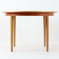 チーク材の天板とオーク材の脚部が美しく調和したこちらの円形エクステンションダイニングテーブルは、デンマーク製ならではの丁寧な仕上げと実用性が魅力の北欧ビンテージ家具です。直径110cmの円形天板は、中央に拡張板を2枚追加することで広々としたオーバル型に変化し、来客時やホームパーティーなどにも柔軟に対応できます。細身のテーパー脚が軽やかな印象を与え、温かみのある木の表情が空間に自然と溶け込む逸品です。