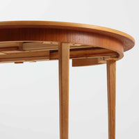 チーク材の天板とオーク材の脚部が美しく調和したこちらの円形エクステンションダイニングテーブルは、デンマーク製ならではの丁寧な仕上げと実用性が魅力の北欧ビンテージ家具です。直径110cmの円形天板は、中央に拡張板を2枚追加することで広々としたオーバル型に変化し、来客時やホームパーティーなどにも柔軟に対応できます。細身のテーパー脚が軽やかな印象を与え、温かみのある木の表情が空間に自然と溶け込む逸品です。