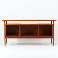 カイ・クリスチャンセンがデザインし、FM furniture社によって製造されたこちらの両袖デスクは、チーク材の美しい木目と温かみのある色合いが魅力の北欧ビンテージ家具です。左右には3杯ずつの引き出し、中央には扉付き収納を備え、背面にはオープンシェルフが設けられており、デスクとしての高い収納力と機能性を誇ります。壁付けはもちろん、間仕切りとしても活用できるため、空間の中心にも映える設計です。丸みを帯びた取手や脚部など、細部にまでこだわった意匠は、カイ・クリスチャンセンらしい洗練された美しさを体現しており、上質なワークスペースを演出します。