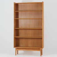 Johannes Sorthがデザインし、Bornholms Mobelfabrik社から1965年に製造されたこちらのブックシェルフは、美しい木目のオーク材と縦長のすっきりとしたフォルムが印象的な北欧ビンテージ家具で、豊富な棚板が本や雑貨の収納に優れた実用性を発揮します。裏面には「29 JUNI 1965」の刻印が残されており、当時のクラフトマンシップを感じさせる趣深い一台です。