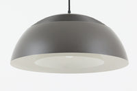 アルネ・ヤコブセンによってデザインされ、Louis Poulsen(ルイスポールセン)より製造されたAJロイヤル ペンダントライト。こちらは希少なグラファイトグレーカラーで、落ち着いたトーンが空間にシックな雰囲気を演出します。直径50cmの大型サイズで、光源を遮る構造と放射状に配置されたルーバーにより、眩しさを抑えた柔らかい光が空間全体を包み込みます。点灯時には上部のスリットから漏れる光も美しく、デザイン性と機能性を兼ね備えた一品です。外観には小傷や使用感がありますが、ビンテージならではの風合いとしてお楽しみいただけます。