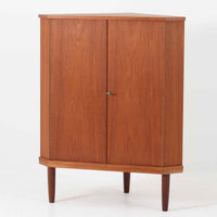 三角形のユニークなフォルムが目を引くこちらのコーナーキャビネットは、デンマーク製の北欧ビンテージ家具です。チーク材の温もりある木肌と、鍵付きのシンメトリーな扉が上品な佇まいを演出します。内部には棚板が2枚設けられており、日用品や雑貨などの収納に実用的。空間の角にすっきりと収まる設計は、デッドスペースを活かしながら、インテリアに程よいアクセントを加えてくれます。シンプルながら希少性を感じさせる一台です。