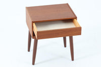 デンマークで製造されたヴィンテージのサイドチェスト。温もりのあるチーク材を用いた本体に、先細りの丸脚を組み合わせた軽やかな佇まいが魅力です。引き出し1杯に加え、下部にはオープンスペースを備えており、リモコンや文庫本などをすぐに取り出せる実用的な構造。天板や側面にはすっきりとした面取りが施され、シンプルなデザインの中に丁寧な仕事が感じられます。北欧らしいあたたかみと実用性を兼ね備えた一台。ベッドサイドはもちろん、リビングや玄関先など、暮らしのさまざまな場面で活躍します。