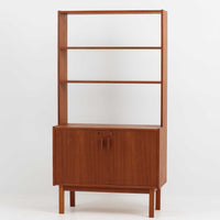 スウェーデンのBreox Mobler社製によるチーク材オープンシェルフで、幅85cmと使いやすいサイズ感の北欧ビンテージ家具です。上部は3段のオープン棚で書籍やオブジェを美しく飾ることができ、下部には鍵付き扉の収納スペースを備えており、実用性とデザイン性を兼ね備えています。直線的で軽やかなフレーム構造が北欧らしいシンプルな美を感じさせ、経年によるチーク材の深みある色合いがさらに存在感を高めています。リビングや書斎の収納兼ディスプレイとして最適な一台です。