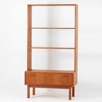 Breox Mobler社によってスウェーデンで製造されたこちらのディスプレイシェルフは、チーク材の温かみある風合いと機能美を兼ね備えた北欧ビンテージ家具です。上段は高さのある3段の棚構成となっており、書籍や小物、アートピースなどを美しく飾るのに適した開放的な設計です。下段には鍵付きのフラップ式収納が備えられ、生活感のあるアイテムをすっきりと隠せる実用的な構造となっています。直線的で軽やかなデザインは圧迫感がなく、省スペースでありながら高い収納力を誇ります。チーク材特有の深みある色合いが魅力で、リビングや書斎、寝室などあらゆる空間に馴染みます。北欧ビンテージ家具ならではの経年変化と上質な存在感をお楽しみいただけます。