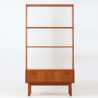 Breox Mobler社によってスウェーデンで製造されたこちらのディスプレイシェルフは、チーク材の温かみある風合いと機能美を兼ね備えた北欧ビンテージ家具です。上段は高さのある3段の棚構成となっており、書籍や小物、アートピースなどを美しく飾るのに適した開放的な設計です。下段には鍵付きのフラップ式収納が備えられ、生活感のあるアイテムをすっきりと隠せる実用的な構造となっています。直線的で軽やかなデザインは圧迫感がなく、省スペースでありながら高い収納力を誇ります。チーク材特有の深みある色合いが魅力で、リビングや書斎、寝室などあらゆる空間に馴染みます。北欧ビンテージ家具ならではの経年変化と上質な存在感をお楽しみいただけます。