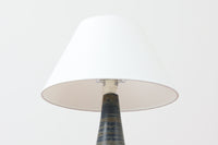 デンマーク・ボーンホルム島の名窯michael Andersen & Sonによるテーブルランプ。八角形のシャープなフォルムと、マットな質感の釉薬のコントラストが美しい一点です。落ち着いたブルーグレーのトーンがインテリアに静かなアクセントを添えてくれます。高さは約50cmとやや大きめで、程よい存在感があり、サイドボードやコンソールの上などにもおすすめです。シェードは新品のリネン製。