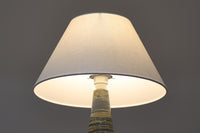 デンマーク・ボーンホルム島の名窯michael Andersen & Sonによるテーブルランプ。八角形のシャープなフォルムと、マットな質感の釉薬のコントラストが美しい一点です。落ち着いたブルーグレーのトーンがインテリアに静かなアクセントを添えてくれます。高さは約50cmとやや大きめで、程よい存在感があり、サイドボードやコンソールの上などにもおすすめです。シェードは新品のリネン製。