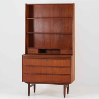 チーク材の温もりが魅力のこちらのディスプレイシェルフは、引き出し収納と棚が一体となった北欧ビンテージらしい実用性と美しさを兼ね備えた一台で、下段には鍵付きの3杯引き出し、上段には棚が3段設けられており、書斎やリビングの収納兼飾り棚としてはもちろん、店舗什器としても活躍します。細身の丸脚が全体に軽やかな印象を与え、チーク材特有の深みのある色合いと経年による艶が上質な雰囲気を醸し出しています。