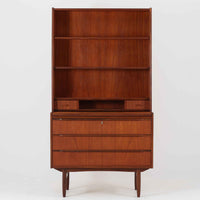 チーク材の温もりが魅力のこちらのディスプレイシェルフは、引き出し収納と棚が一体となった北欧ビンテージらしい実用性と美しさを兼ね備えた一台で、下段には鍵付きの3杯引き出し、上段には棚が3段設けられており、書斎やリビングの収納兼飾り棚としてはもちろん、店舗什器としても活躍します。細身の丸脚が全体に軽やかな印象を与え、チーク材特有の深みのある色合いと経年による艶が上質な雰囲気を醸し出しています。