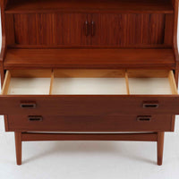 Johannes Sorth(ヨハネス・ソース)によるNexo Mobelfabrik社製のチーク材ディスプレイシェルフです。幅100cmと程よいサイズ感で、上段の棚は高さのある書籍やオブジェを飾るのに適しており、中央の蛇腹扉の内側には小引き出しや仕切りが備わり、細かな収納にも対応します。下段の3杯の引き出しは収納力に優れ、衣類や書類の整理に便利です。直線的なフォルムに温かみのあるチーク材の木目が映え、経年の艶が深みを増したビンテージらしい風合いを楽しめます。機能性と美観を兼ね備えた北欧家具の魅力が詰まった一台です。