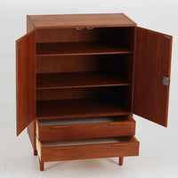 デンマーク製の収納キャビネットです。上段には観音開きの扉内に可動棚が設けられており、食器や書類をすっきりと整理できます。内部まで丁寧に仕上げられており、扉を開けてお気に入りの器やオブジェを飾る“見せる収納”としても楽しめます。扉には鍵が付属しており、大切なものを安全に保管することも可能です。下段には2杯の引き出しが備わり、小物類や日用品の収納にも便利。チーク材の豊かな木目と深みのある色合いが美しく、北欧家具らしい温もりを感じさせます。脚部のテーパー形状が全体を軽やかに見せ、シンプルながら上質な存在感を放つ一台です。