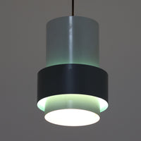 Jo HammerborgがFog & Morup社のためにデザインした「Central」ペンダントライトです。直径23cmのコンパクトなサイズながら、スチール製の二重シリンダー構造が特徴的で、点灯時には上下から光が広がり独特の陰影を演出します。外側のグレーと内側のホワイトがコントラストを生み、点灯時にはほのかなグリーンの光が漏れ出す美しいデザインです。ダイニングや小スペースに適したサイズで、北欧モダンのエッセンスを感じさせるビンテージ照明です。シェードの内側に施されたグリーンの塗装が、点灯時に柔らかなニュアンスを加え、空間に独特の雰囲気を演出します。