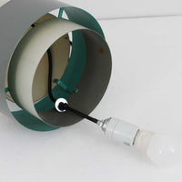 Jo HammerborgがFog & Morup社のためにデザインした「Central」ペンダントライトです。直径23cmのコンパクトなサイズながら、スチール製の二重シリンダー構造が特徴的で、点灯時には上下から光が広がり独特の陰影を演出します。外側のグレーと内側のホワイトがコントラストを生み、点灯時にはほのかなグリーンの光が漏れ出す美しいデザインです。ダイニングや小スペースに適したサイズで、北欧モダンのエッセンスを感じさせるビンテージ照明です。シェードの内側に施されたグリーンの塗装が、点灯時に柔らかなニュアンスを加え、空間に独特の雰囲気を演出します。