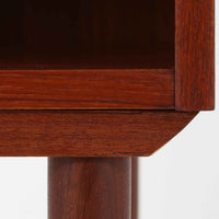 チーク材の豊かな木目が美しいこちらのサイドチェストは、北欧ビンテージらしい端正なデザインと実用性を兼ね備えた一台です。天板の縁には立ち上がりが施され、小物の転落を防ぐ工夫がされています。引き出し下のオープンスペースは本や雑貨の収納に便利で、ソファやベッドサイドに置けばサイドテーブルとしても活躍します。丸みを帯びた持ち手やテーパードレッグが柔らかな印象を与え、経年変化による木肌の深みが空間に温もりを添える逸品です。