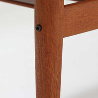 Grete Jalkがデザインし、Glostrup Mobelfabrikで製作されたこちらのセンターテーブルは、端正なプロポーションと軽やかな構造が魅力の北欧ビンテージ品です。幅160cmのゆとりある天板下にはスラット状の棚板を備え、雑誌やブランケットなどを整理しながら使える実用性も兼ね備えています。丸みを帯びた脚部や天板縁の丁寧な仕上げからは、女性デザイナーらしい繊細な美意識と当時の高い木工技術が感じられ、経年により深みを増した木肌が空間に落ち着いた存在感をもたらします。