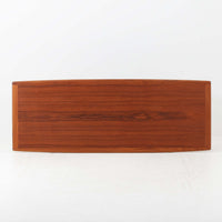 Grete Jalkがデザインし、Glostrup Mobelfabrikで製作されたこちらのセンターテーブルは、端正なプロポーションと軽やかな構造が魅力の北欧ビンテージ品です。幅160cmのゆとりある天板下にはスラット状の棚板を備え、雑誌やブランケットなどを整理しながら使える実用性も兼ね備えています。丸みを帯びた脚部や天板縁の丁寧な仕上げからは、女性デザイナーらしい繊細な美意識と当時の高い木工技術が感じられ、経年により深みを増した木肌が空間に落ち着いた存在感をもたらします。