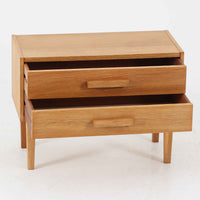 オーク材を用いたこちらの2段チェストは、北欧ビンテージ家具らしいシンプルかつ機能的なデザインが魅力です。直線的なフォルムに対し、細身でテーパーのかかった脚部が軽やかな印象を与え、空間を圧迫せずに置くことができます。幅60cmとコンパクトながら、2杯の引き出しは日用品や小物収納に便利で、ベッドサイドやリビングの補助収納としても最適です。経年により深みを増したオークの木肌が、温もりある雰囲気を演出する一点物です。