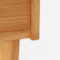 オーク材を用いたこちらの2段チェストは、北欧ビンテージ家具らしいシンプルかつ機能的なデザインが魅力です。直線的なフォルムに対し、細身でテーパーのかかった脚部が軽やかな印象を与え、空間を圧迫せずに置くことができます。幅60cmとコンパクトながら、2杯の引き出しは日用品や小物収納に便利で、ベッドサイドやリビングの補助収納としても最適です。経年により深みを増したオークの木肌が、温もりある雰囲気を演出する一点物です。