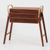 こちらのソーイングボックスは、チーク材とビーチ材を組み合わせた軽やかな構成が魅力の北欧ビンテージ品で、トップのフラップを開くと段違いに展開するトレイと下段の引き出しが現れる優れた収納構造を備え、裁縫道具や小物を効率よく整理できます。柔らかく曲げられた左右のビーチ材の持ち手がアクセントとなり、職人技の感じられる繊細な作りと経年で深まった木肌の風合いが空間に温かな存在感をもたらします。リビングやワークスペースのサイドテーブルとしても実用的にお使いいただけます。