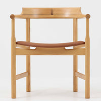 Hans J. Wegnerが1975年にデザインし、PP Mobler社が製造したPP52 Captain's Chairは、背からアームまで滑らかにつながる一体成型の美しいフォルムが魅力のアームチェアです。素材には木目の美しいアッシュ材と本革が用いられ、背面には象徴的な埋木の意匠が施されています。座面はゆったりとしたカーブで快適な座り心地を実現し、ダイニングからデスクシーンまで幅広く対応します。現在も製造されており、現行品の販売価格は約90~100万円程度となっています。