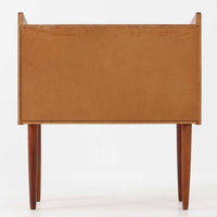 チーク材を使用したデンマーク製の3段チェストで、直線的な本体に対して丸みを帯びた引き手と細身のテーパードレッグが柔らかな印象を与え、さらに天板左右に伸びた耳のような張り出しがデザインのアクセントとなり、北欧らしい優雅な佇まいが感じられます。引き出しは3杯備え、衣類や小物収納に適したサイズ感で、ベッドサイドやリビングの一角に置きやすく、花器や照明のディスプレイ台としても楽しめます。シンプルな造形ながら木目の美しさが際立ち、空間に温かみと落ち着きを添えてくれるビンテージ家具です。