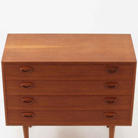 カイ・クリスチャンセンが手掛け、フェルドバレス・モーベルファブリック社によって製作された4段チェストは、北欧ビンテージらしい端正な佇まいと高い実用性を兼ね備えた一台です。良質なチーク材を用いた本体は、木目の美しさが前面に表れ、半円状に削り出された取手や細身のテーパードレッグが、全体に軽やかで洗練された印象を与えています。引き出しは深さにゆとりがあり収納力も十分で、衣類や小物の整理に最適です。経年変化によって深みを増したチークの色合いが空間に温もりを添え、リビングや寝室、書斎など幅広いシーンで主役として活躍します。