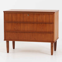 デンマーク製のチーク材3段チェストです。前板の一体的なデザインが美しく、取手部分を削り出した滑らかなラインが上品な印象を与えます。幅が77cmと少し大きめで、コンパクトながら収納力があり、寝室や玄関、リビングのサイド収納としても活躍します。最上段には鍵付きの引き出しが設けられ、大切な書類や貴重品の保管にも便利です。脚部まで丁寧に仕上げられた造りは北欧家具ならではの職人技を感じさせ、空間に温もりを添えてくれます。