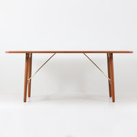 Borge Mogensenがデザインし、Soborg Mobler社より製造されたダイニングテーブル「BM1160」ハンティングテーブルです。現行品はカール・ハンセン社からも展開されていますが、こちらはSoborg社製造によるビンテージ品で、現在では入手が難しいチーク材仕様となっています。幅180cmと現行品よりややコンパクトなサイズ感で、日本の住空間にも取り入れやすい設計です。豊かな木目を持つチーク材の天板に、脚部を支える真鍮製クロスバーを組み合わせることで、堅牢さと美しさを兼ね備えています。角には滑らかな曲線が施され、温かみのある印象を添えつつ、家族や来客を迎える食卓として十分な広さを誇ります。真鍮パーツは構造的強度を高めると同時にビンテージらしい上質なアクセントとなり、シンプルでありながら存在感ある佇まいを演出。北欧家具ならではの実用性とデザイン性が息づき、年月を重ねることでさらに素材の風合いが深まり、空間を豊かに彩ります。