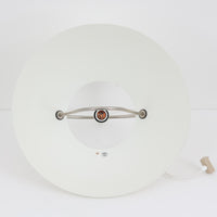 Pandul(パンドゥル)社が正規製造している、ハンス・J・ウェグナー(Hans J. Wegner)デザインのペンダントライト「JH604」です。1960年代にLouis Poulsen(ルイスポールセン)社で製造されていたモデルで、ウェグナーが自邸のためにデザインしたことでも知られています。直径50cmの存在感あるフォルムと、アルミ製シェードとステンレス製アームによる軽やかで堅牢な構造は、北欧デザインらしい機能美を体現。点灯時には下方向だけでなくシェード上部の隙間からも光が柔らかく漏れ、空間に奥行きを与えます。Pandulは1982年にデンマークで設立され、Louis Poulsenから受け継いだ名作を当時のデザインと品質を尊重して製造しているブランドです。なお、本品はプラスチック製コードリールが欠品しておりますが、全体として良好なコンディションを保っています。ヴィンテージデザインの魅力と現行製造ならではの安心感を兼ね備えた、北欧デザインを象徴する一灯です。