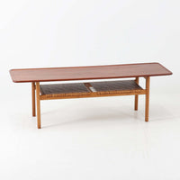 Hans J. WegnerがAndreas Tuckのために手掛けたAT10センターテーブルは、チーク材の天板にオーク材のフレーム、ラタン張りの棚板を組み合わせた、素材使いの美しさが際立つ北欧ビンテージの名作です。直線を基調とした端正なプロポーションの中に、天板縁のやわらかな丸みや、軽やかに抜け感を生むラタン棚が配され、視覚的にも圧迫感のない佇まいに仕上げられています。幅160cmのゆとりあるサイズはリビングの主役として使いやすく、雑誌や小物を収納できる実用性も備え、経年変化により深みを増した木肌が空間に上質な落ち着きをもたらします。なお、天板には反りがあり、大きめのへこみも見られるため、その点を考慮した価格設定としておりますが、ご使用には問題なく、ビンテージならではの風合いとしてご理解いただける方におすすめの一台です。