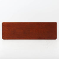 Hans J. WegnerがAndreas Tuckのために手掛けたAT10センターテーブルは、チーク材の天板にオーク材のフレーム、ラタン張りの棚板を組み合わせた、素材使いの美しさが際立つ北欧ビンテージの名作です。直線を基調とした端正なプロポーションの中に、天板縁のやわらかな丸みや、軽やかに抜け感を生むラタン棚が配され、視覚的にも圧迫感のない佇まいに仕上げられています。幅160cmのゆとりあるサイズはリビングの主役として使いやすく、雑誌や小物を収納できる実用性も備え、経年変化により深みを増した木肌が空間に上質な落ち着きをもたらします。なお、天板には反りがあり、大きめのへこみも見られるため、その点を考慮した価格設定としておりますが、ご使用には問題なく、ビンテージならではの風合いとしてご理解いただける方におすすめの一台です。