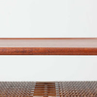 Hans J. WegnerがAndreas Tuckのために手掛けたAT10センターテーブルは、チーク材の天板にオーク材のフレーム、ラタン張りの棚板を組み合わせた、素材使いの美しさが際立つ北欧ビンテージの名作です。直線を基調とした端正なプロポーションの中に、天板縁のやわらかな丸みや、軽やかに抜け感を生むラタン棚が配され、視覚的にも圧迫感のない佇まいに仕上げられています。幅160cmのゆとりあるサイズはリビングの主役として使いやすく、雑誌や小物を収納できる実用性も備え、経年変化により深みを増した木肌が空間に上質な落ち着きをもたらします。なお、天板には反りがあり、大きめのへこみも見られるため、その点を考慮した価格設定としておりますが、ご使用には問題なく、ビンテージならではの風合いとしてご理解いただける方におすすめの一台です。