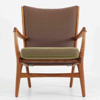 Hans J. Wegner(ハンス・J・ウェグナー)によるイージーチェア「AP16」。デンマークの名門AP stolen社より製造された一脚です。緩やかに傾斜した背もたれと、滑らかに削り出されたアームの曲線が美しく調和し、オーク材の力強い木目と職人技が際立ちます。背面にはブラウン、座面にはグリーンストライプの張地を採用し、上品ながらも温かみのある印象を与えます。現地デンマークのオークションで入手した確かな出自を持つ本品は、読書やくつろぎの時間をより豊かなものにしてくれます。経年による木部の風合いがさらに深みを加えています。