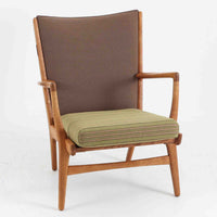 Hans J. Wegner(ハンス・J・ウェグナー)によるイージーチェア「AP16」。デンマークの名門AP stolen社より製造された一脚です。緩やかに傾斜した背もたれと、滑らかに削り出されたアームの曲線が美しく調和し、オーク材の力強い木目と職人技が際立ちます。背面にはブラウン、座面にはグリーンストライプの張地を採用し、上品ながらも温かみのある印象を与えます。現地デンマークのオークションで入手した確かな出自を持つ本品は、読書やくつろぎの時間をより豊かなものにしてくれます。経年による木部の風合いがさらに深みを加えています。