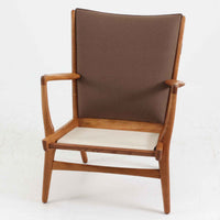 Hans J. Wegner(ハンス・J・ウェグナー)によるイージーチェア「AP16」。デンマークの名門AP stolen社より製造された一脚です。緩やかに傾斜した背もたれと、滑らかに削り出されたアームの曲線が美しく調和し、オーク材の力強い木目と職人技が際立ちます。背面にはブラウン、座面にはグリーンストライプの張地を採用し、上品ながらも温かみのある印象を与えます。現地デンマークのオークションで入手した確かな出自を持つ本品は、読書やくつろぎの時間をより豊かなものにしてくれます。経年による木部の風合いがさらに深みを加えています。