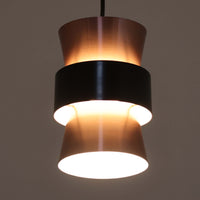 Jo HammerborgがFog & Morup社のためにデザインした直径14cmの小ぶりなペンダントライトです。アルミ製のシェードは上下に広がる砂時計のようなフォルムに、中央のブラックバンドがアクセントとなったモダンなデザイン。点灯時には光が上下にやわらかく広がり、陰影の美しい表情を見せます。コンパクトサイズのためダイニングで複数吊り下げての使用や、玄関・書斎のポイントライトとしても活躍。北欧ビンテージ照明ならではの洗練された存在感を放ちます。