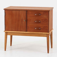 デンマーク製の小ぶりなキャビネットです。チーク材をメインに、オーク材やビーチ材を組み合わせることで、温かみのある色調と軽快な雰囲気を併せ持っています。左側は扉付き収納、右側には3杯の引き出しを備え、実用性とデザイン性を両立。丸みを帯びた取っ手や脚部のテーパーラインが北欧家具らしい柔らかな印象を与えます。幅63cmとコンパクトなサイズで、リビングや寝室、玄関など限られたスペースでも活躍する、ビンテージならではの風合いを持つ一台です。