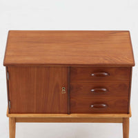デンマーク製の小ぶりなキャビネットです。チーク材をメインに、オーク材やビーチ材を組み合わせることで、温かみのある色調と軽快な雰囲気を併せ持っています。左側は扉付き収納、右側には3杯の引き出しを備え、実用性とデザイン性を両立。丸みを帯びた取っ手や脚部のテーパーラインが北欧家具らしい柔らかな印象を与えます。幅63cmとコンパクトなサイズで、リビングや寝室、玄関など限られたスペースでも活躍する、ビンテージならではの風合いを持つ一台です。