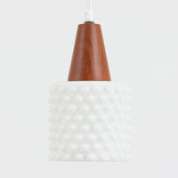 デンマーク製のペンダントライト、直径13cmです。ガラスシェードには立体的なドット模様が施され、点灯すると陰影が浮かび上がり独特の表情を生み出します。上部にはチーク材が用いられ、ガラスの繊細さと木の温もりが調和した北欧らしい意匠が魅力です。小ぶりなサイズながらも存在感があり、キッチンや廊下、ベッドサイドなど複数使いにも適しています。経年による素材の風合いがビンテージ品ならではの味わいを感じさせ、日常空間に個性を添える一品です。