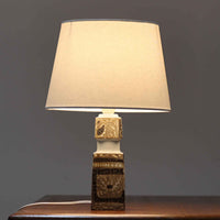 Nils Thorssonがデザインし、Royal Copenhagen社から発表された「BACA」シリーズのテーブルランプは、高さ39cmのバランスの取れたサイズ感で、北欧ビンテージらしい存在感を放ちます。陶磁器製のベースには細やかな装飾模様が施され、グラフィカルでありながら落ち着いた色調が空間に洗練された雰囲気を添えます。リネンシェードを透過する柔らかな光が温もりを演出し、リビングやベッドサイドに最適です。年月を経て深みを増した質感と工芸的な美しさを楽しめる一点物です。