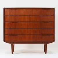 北欧ビンテージらしい端正な佇まいが魅力の5段チェストです。良質な木材を用いた本体は、横に流れる美しい木目に加え、角だけでなく前板を含む本体全体が緩やかな曲線を描く、有機的で上質なフォルムが特徴です。引き出し前板には手掛け一体型の彫り込みが施され、丸みを帯びた造形と相まって柔らかな印象を与えます。高い工作精度が感じられるクオリティの高い一台で、収納力に優れたサイズながら脚付き構造により軽やかさも備え、寝室やリビングの主収納として活躍します。Vordingborg Mobelfabrik社製と伝えられていますが確証はなく、メーカー不詳のビンテージ品としてご紹介します。経年変化によって深みを増した木肌が、空間に上質な存在感をもたらします。