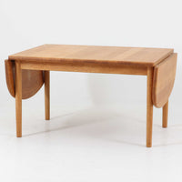Hans J. Wegnerがデザインし、Getama社より製造されたセンターテーブル「GE82」は、丸脚の意匠が特徴で、四角脚の「GE85」と同時期にデザインされたといわれています。バタフライ構造による拡張機能を備えた北欧ビンテージ家具で、オーク無垢材を贅沢に使用し、幅103cmから160cmへと用途に応じてサイズ調整が可能。普段はコンパクトに、来客時には広々と使える実用性が魅力です。シンプルで力強いフォルムと無垢材ならではの豊かな木目は、年月を経て一層の味わいを増し、空間に温もりと存在感を添えます。