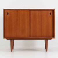 こちらの小ぶりなボードは、温かみのあるチーク材を用いたすっきりとした佇まいが魅力の北欧ビンテージ家具で、スライド扉を開くと左右に棚板付きの収納スペースが現れ、日用品や小物を効率よく整理できます。直線的な箱型の構造に、細身でテーパーの効いた脚部が軽やかな印象を添え、コンパクトながら存在感のある設計が空間に落ち着いたアクセントをもたらします。経年で深まった木肌の質感も味わい深く、リビングや玄関脇のサイド収納としても取り入れやすい一台です。