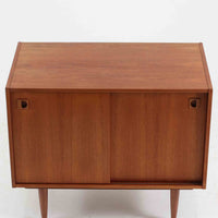 こちらの小ぶりなボードは、温かみのあるチーク材を用いたすっきりとした佇まいが魅力の北欧ビンテージ家具で、スライド扉を開くと左右に棚板付きの収納スペースが現れ、日用品や小物を効率よく整理できます。直線的な箱型の構造に、細身でテーパーの効いた脚部が軽やかな印象を添え、コンパクトながら存在感のある設計が空間に落ち着いたアクセントをもたらします。経年で深まった木肌の質感も味わい深く、リビングや玄関脇のサイド収納としても取り入れやすい一台です。